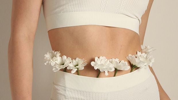 Fragment sylwetki kobiety w białym stroju sportowym; w pasie umieszczone są białe kwiaty symbolizujące delikatność i zdrowie jelit.